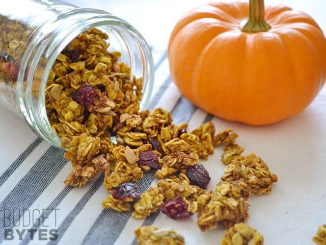 Pumpkin Spice Granola being poured out of mason jar onto counter top, little pumpkin on side for decor 