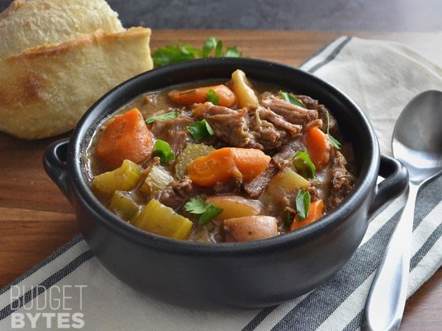 Front view of a bowl of Rosemary Garlic Beef Stew with bread in the background.