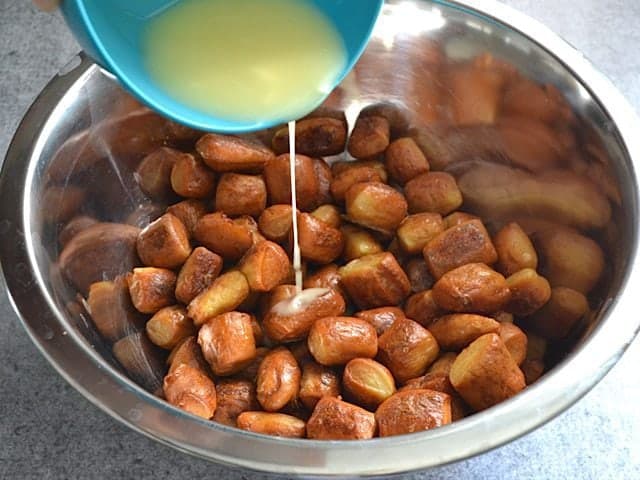 Pouring melted butter over cooked pretzel bites in mixing bowl 