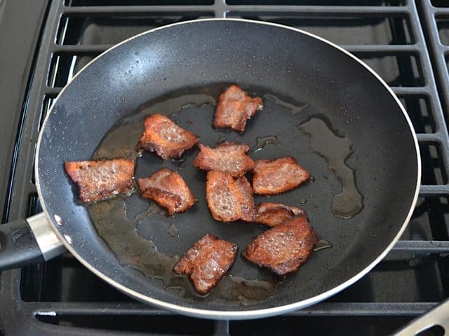 Browned bacon pieces in skillet on stove top 