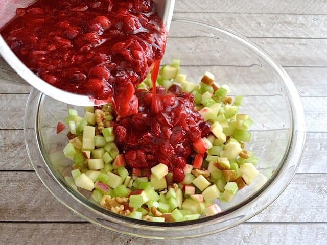 Pouring cooled and cooked cranberries into mixing bowl with apples, celery and walnuts 