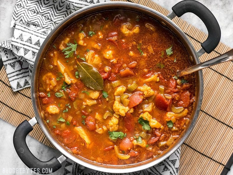 The finished pot of Moroccan Lentil and Vegetable Stew sitting on a bamboo mat with a patterned napkin