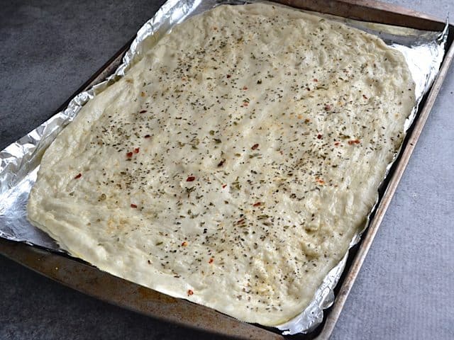 Stretched and seasoned dough placed on baking sheet 