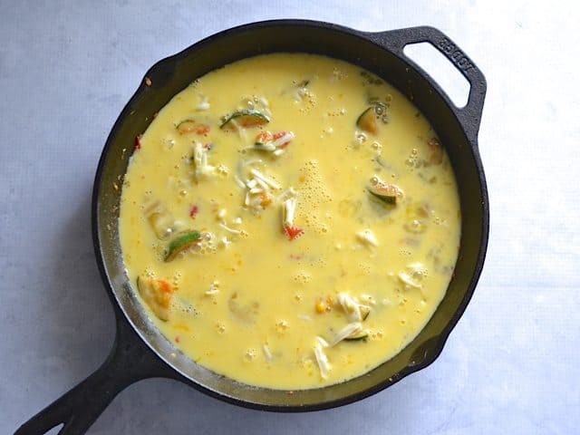 Whisked eggs and milk poured over veggie mixture in skillet 