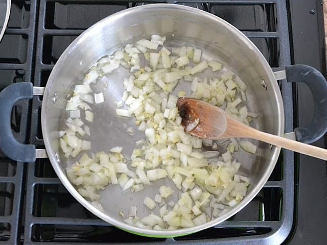 Onion and Garlic in pot being cooked and stirred with wooden spoon