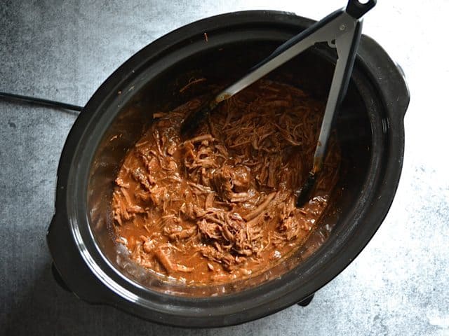 Shredding the Southwest Beef in slow cooker with tongs 