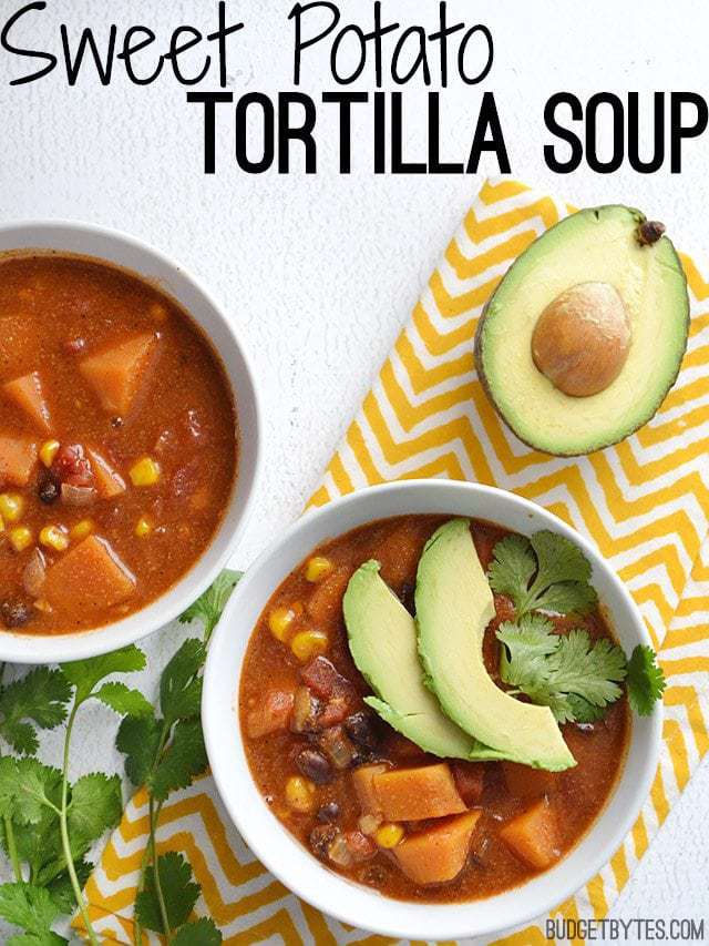Top view of two bowls of Sweet Potato Tortilla Soup, one garnished with avocado and cilantro. Yellow chevron napkin, half an avocado and cilantro on the side for staging. 
