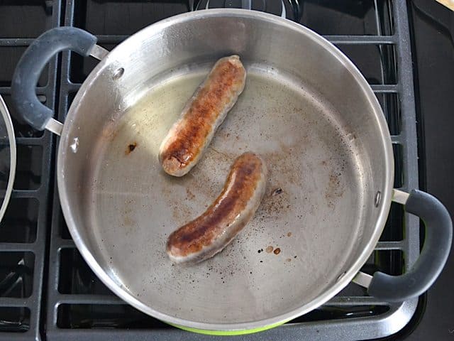 Two sausages in pan browning on stove top 