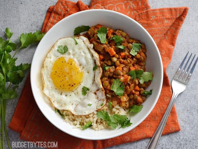 Curried Lentil Bowl (curried lentils, rice and fried egg) sitting on an orange napkin and with a fork on the side 
