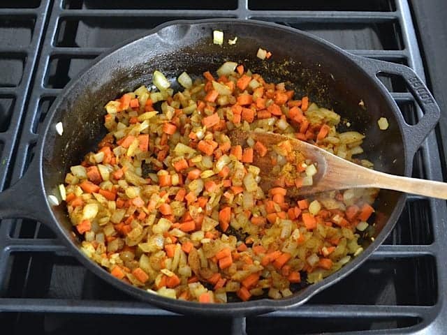 Curry Powder added to veggies in skillet and mixed with wooden spoon 