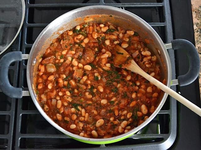 Finished white bean mixture simmering on stove top with wooden spoon 