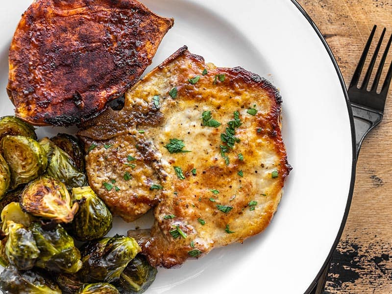 Honey mustard pork chop on a plate with brussels sprouts and sweet potato