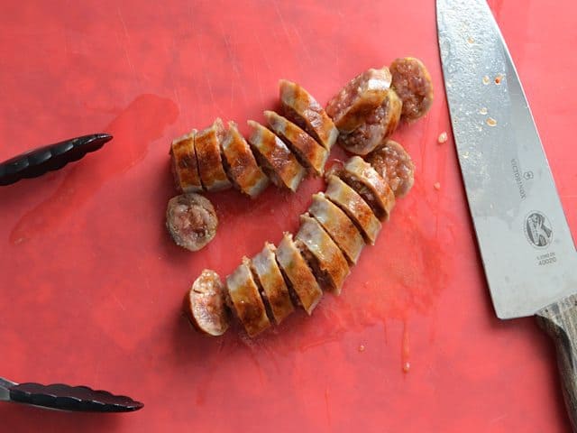 Slicing cooked sausage with knife on cutting board 
