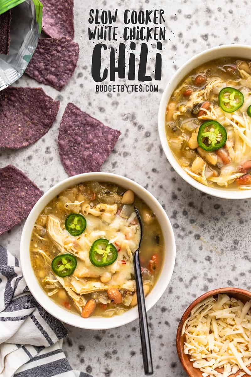 Two bowls of slow cooker white chicken chili with blue corn tortilla chips on the side, title text at the top