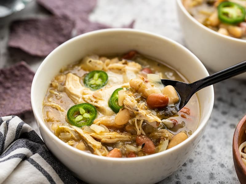 A spoonful of white chicken chili being lifted out of the bowl, blue corn chips in the background