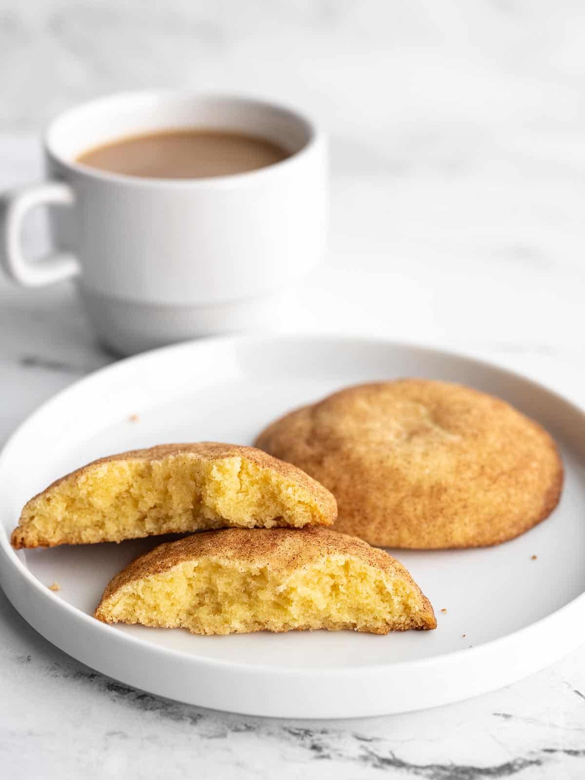 Two snickerdoodles on a plate with a cup of coffee in back