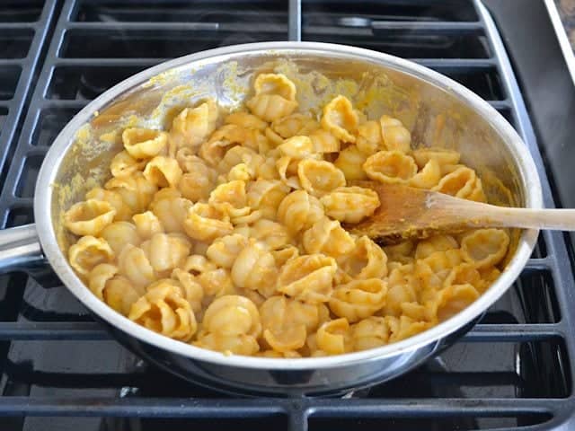 Cooked pasta added into pan with sauce and stirred with wooden spoon 