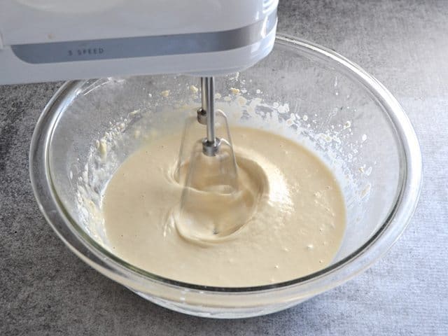 Bread dough mixture being mixed in mixing bowl with hand mixer 