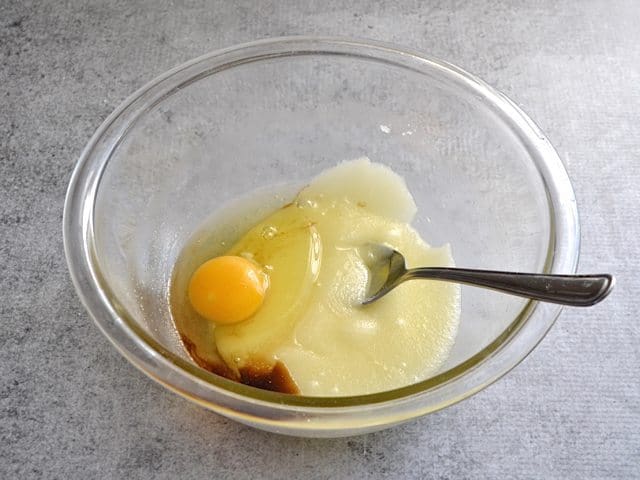 Egg and Vanilla added to mixture in bowl with spoon 