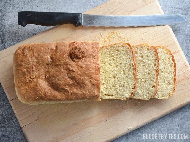 Top view of English Muffin Bread loaf on cutting board with three slices cut off with knife 