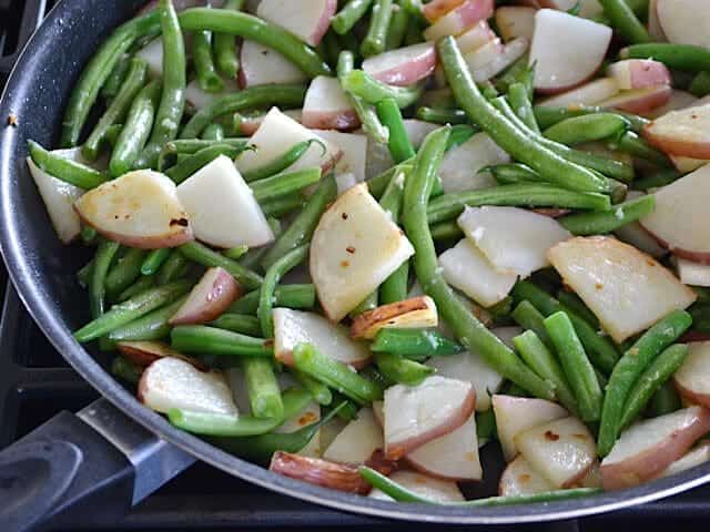 Green beans added to potatoes in skillet 