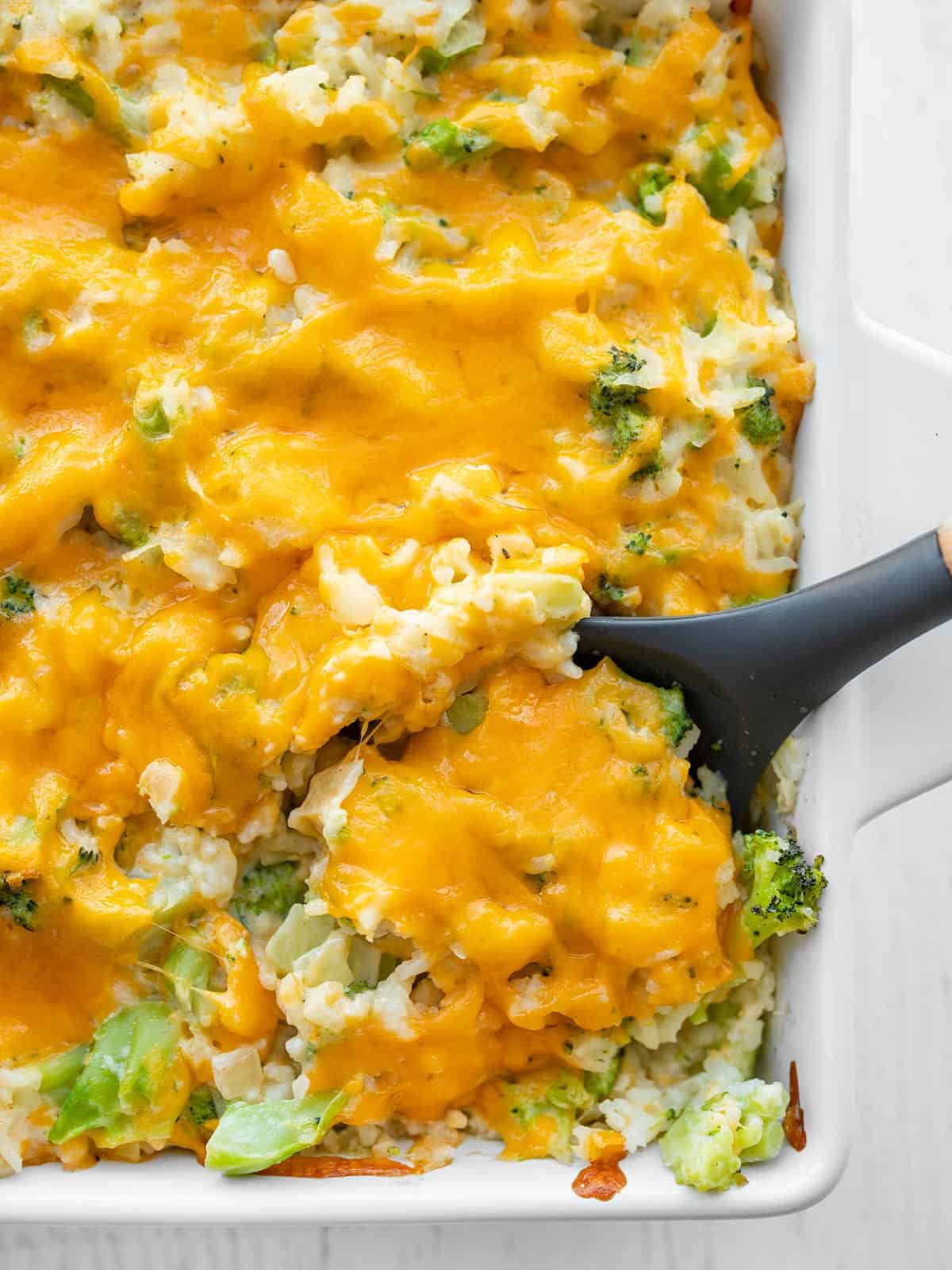 Overhead view of a large spoon scooping some broccoli cheese casserole from the dish