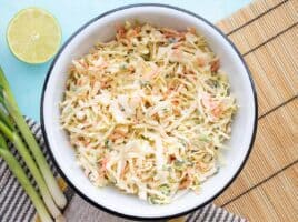 overhead view of a bowl full of cumin lime coleslaw with green onion and limes on the side