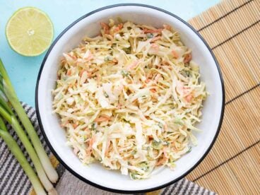 overhead view of a bowl full of cumin lime coleslaw with green onion and limes on the side