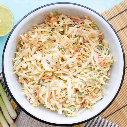 overhead view of a bowl full of cumin lime coleslaw with green onion and limes on the side