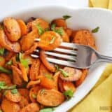 A plate of curry roasted carrots with a fork.