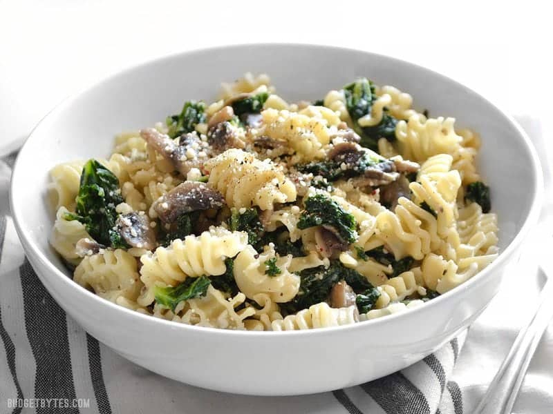 Side view of a bowl of Parmesan & Pepper Kale Pasta sitting on a gray and white stripped napkin 