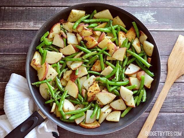 Top view of Skillet Potatoes and Green Beans on costumer top with a wooden spoon and napkin on the side 
