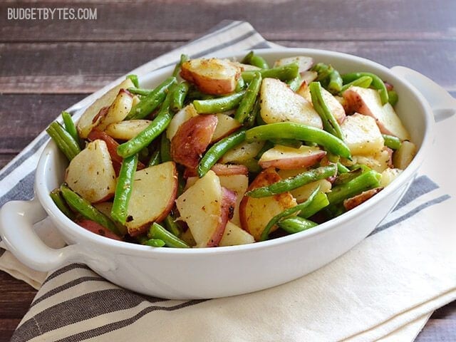 Casserole dish of Skillet Potatoes and Green Beans siting on a gray and white stripped kitchen towel 