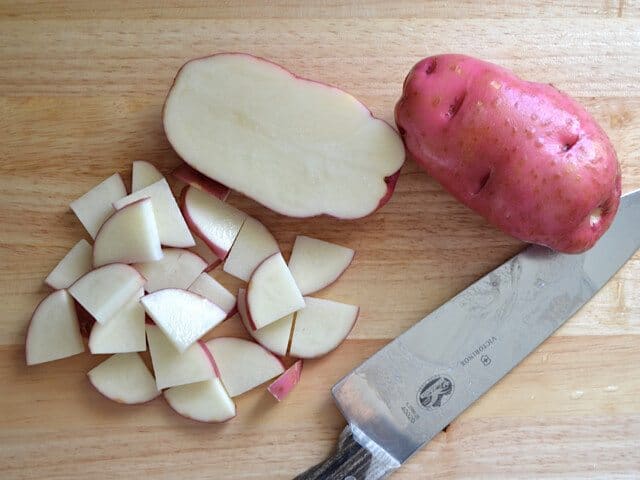 Slicing potatoes with knife on cutting board 