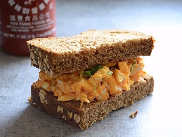 Close up of Sriracha Egg Salad Sandwich, Siracha bottle in the background 