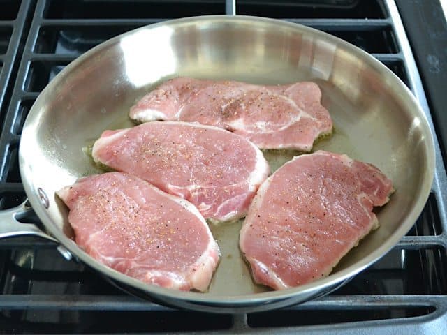 Searing pork chops in skillet on stove top 