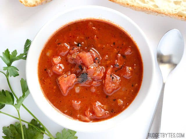 Top view of a bowl of Smoky Tomato Soup with slices of bread and a spoon on the side 
