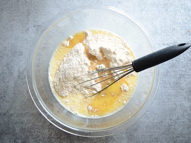 Dry ingredients added to wet ingredients in mixing bowl with whisk 