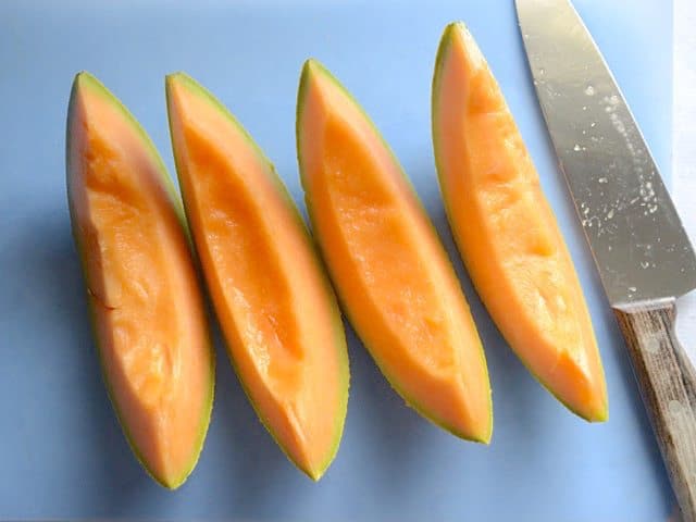 Cantaloupe half cut into quarters with knife 