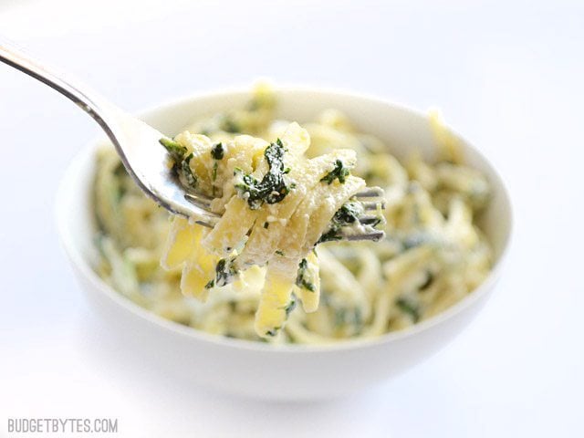 Close up view of a forkful of spinach ricotta pasta being lifted from the serving bowl