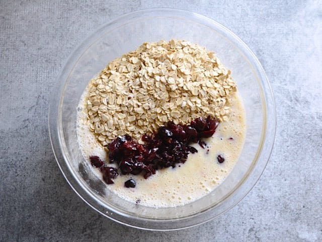 Oats and Cherries stirred into wet ingredients in mixing bowl 