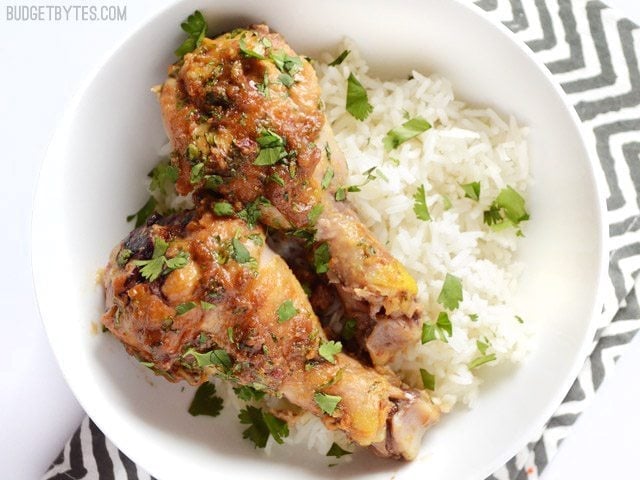 Plate with two drumsticks of Thai Peanut Chicken and a side of rice, sitting on a gray and white chevron napkin 