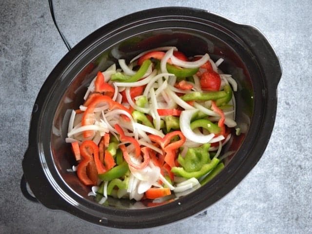 Sliced peppers and onion added to chicken in slow cooker 