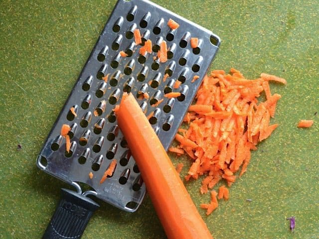 Carrot being shredded on a cheese grater