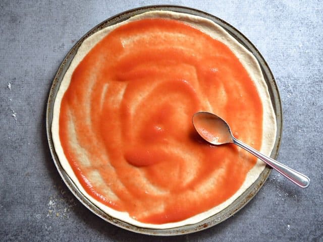 pizza sauce being spread on dough
