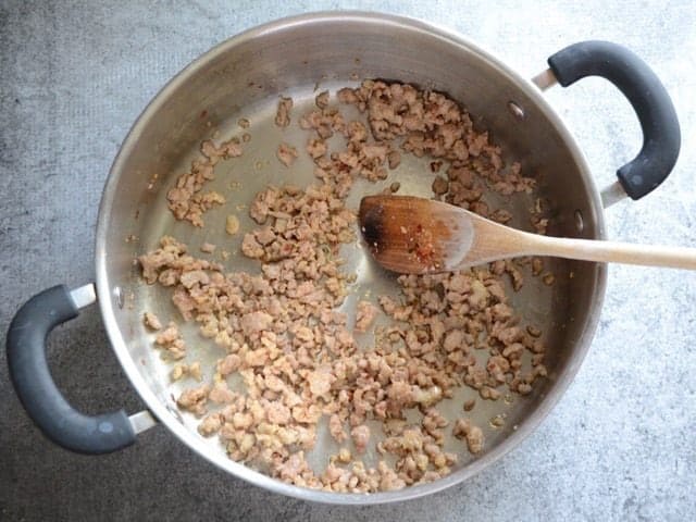 Browned Sausage in a large pot with a wooden spoon