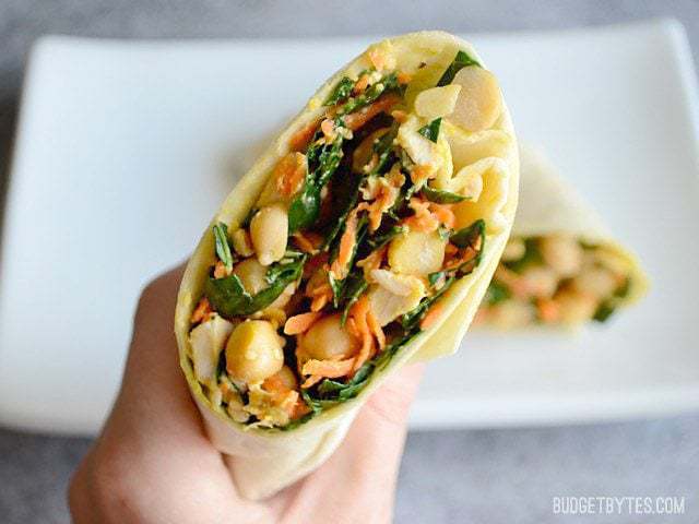 A hand holding half of a kale chicken caesar wrap close to the camera