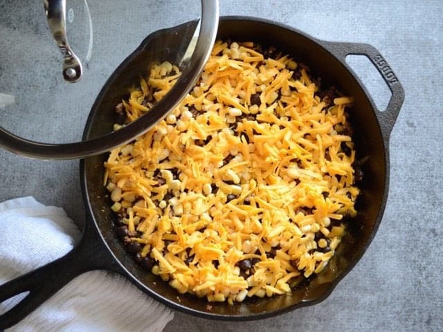 Corn and Cheddar added to the skillet with a lid being placed on the skillet