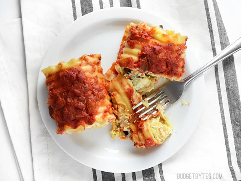 Two vegetable lasagna roll ups on a plate, one cut with a fork