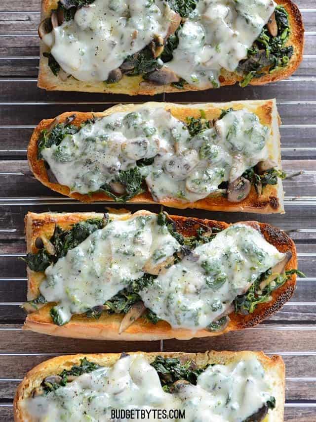 Spinach mushroom french bread pizzas lined up on a wire cooling rack from above